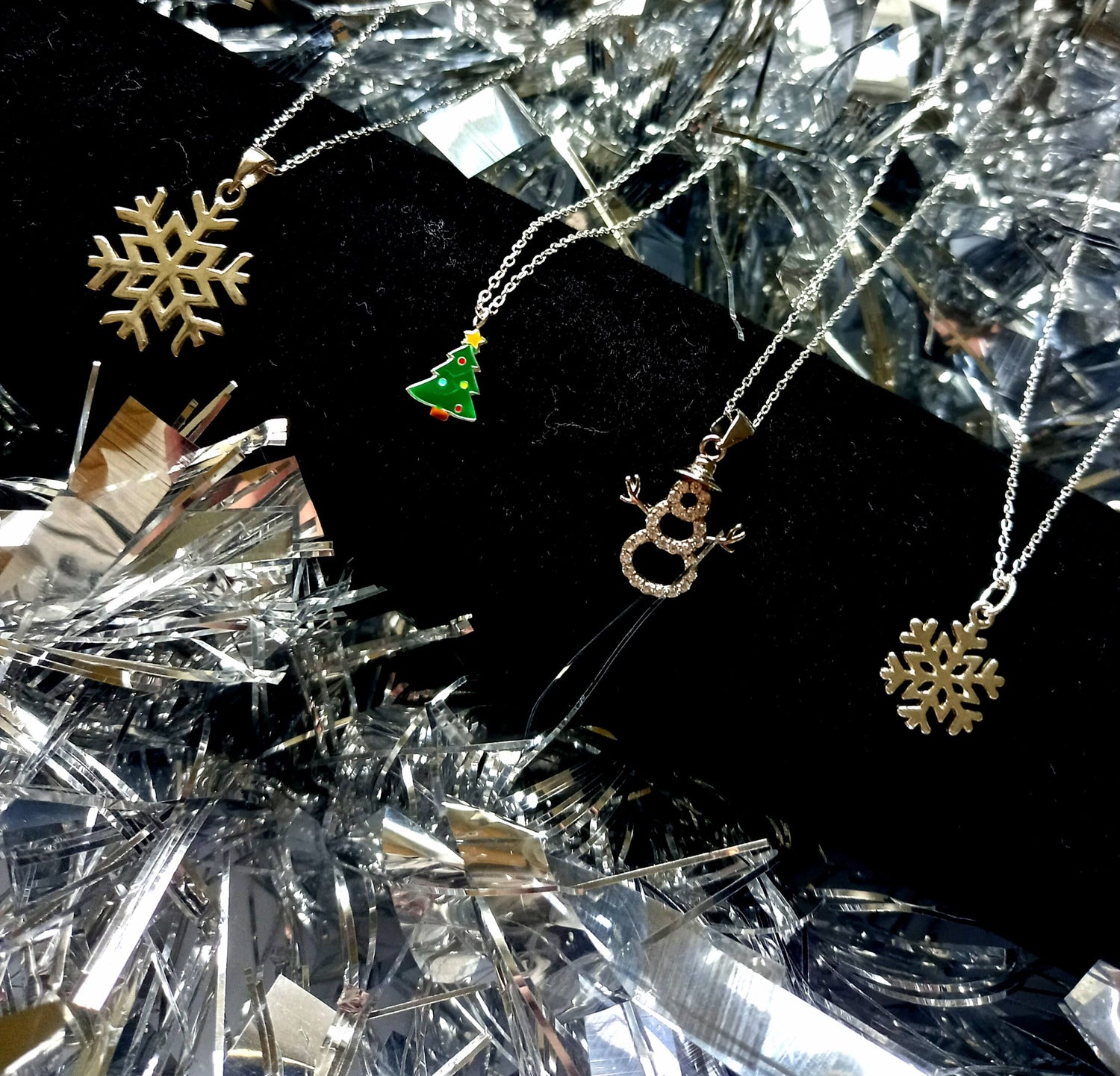 A selection of Christmas themed sterling silver necklaces resting on a black stand on a silver tinsel background