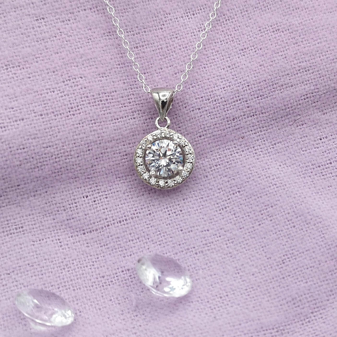 White gold and diamond halo necklace on a purple napkin