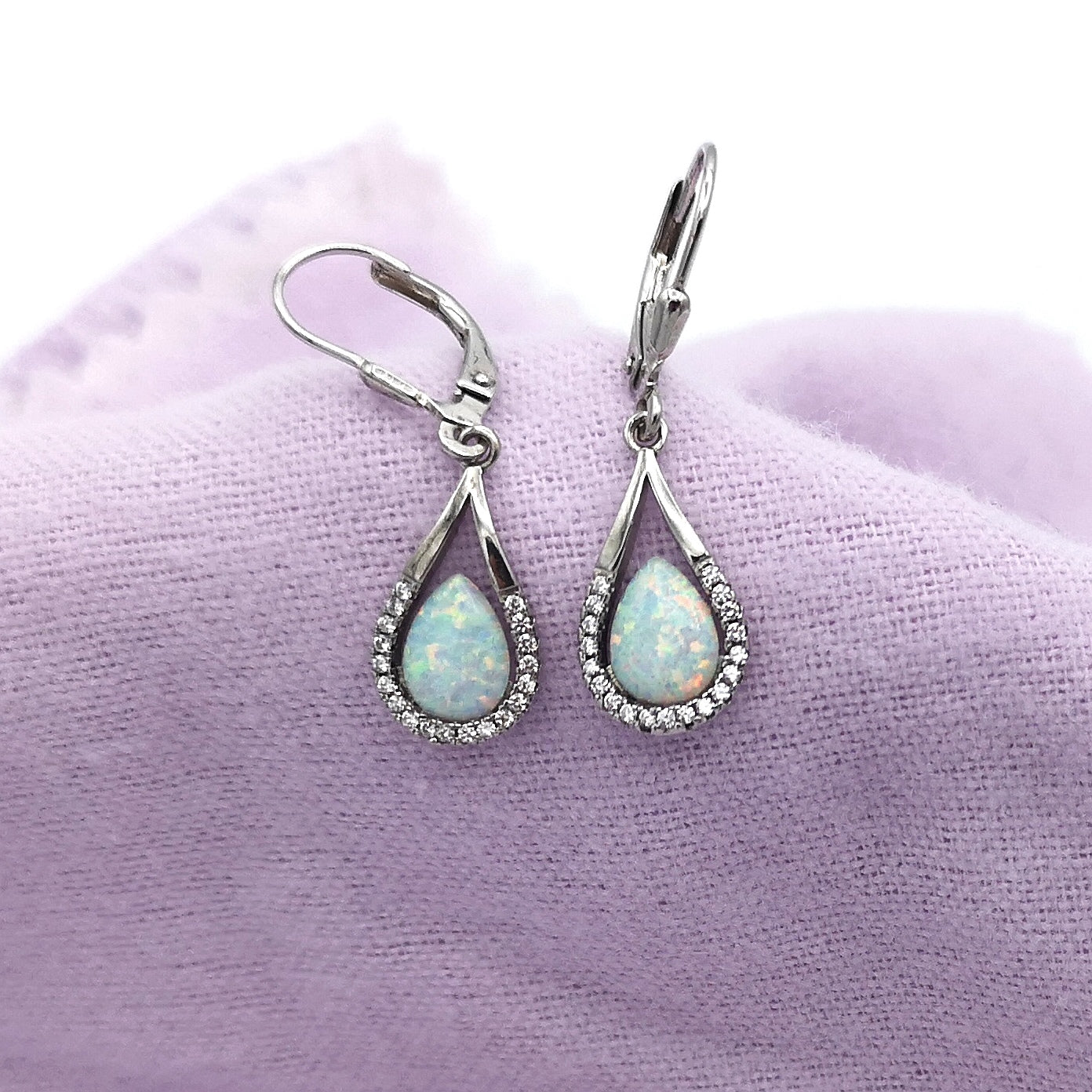 A pair of silver pear cut opal and cz halo drop earrings on a purple napkin
