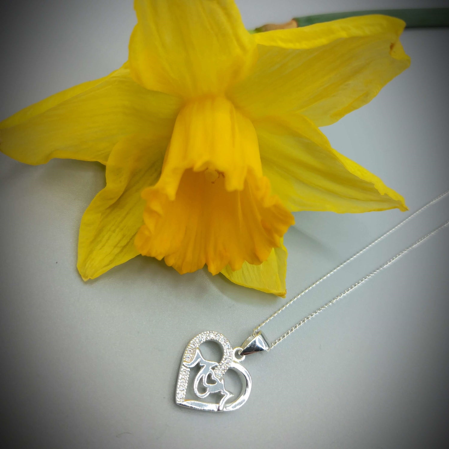 Sterling silver and cz mum pendant on a white background resting in front of a yellow flower